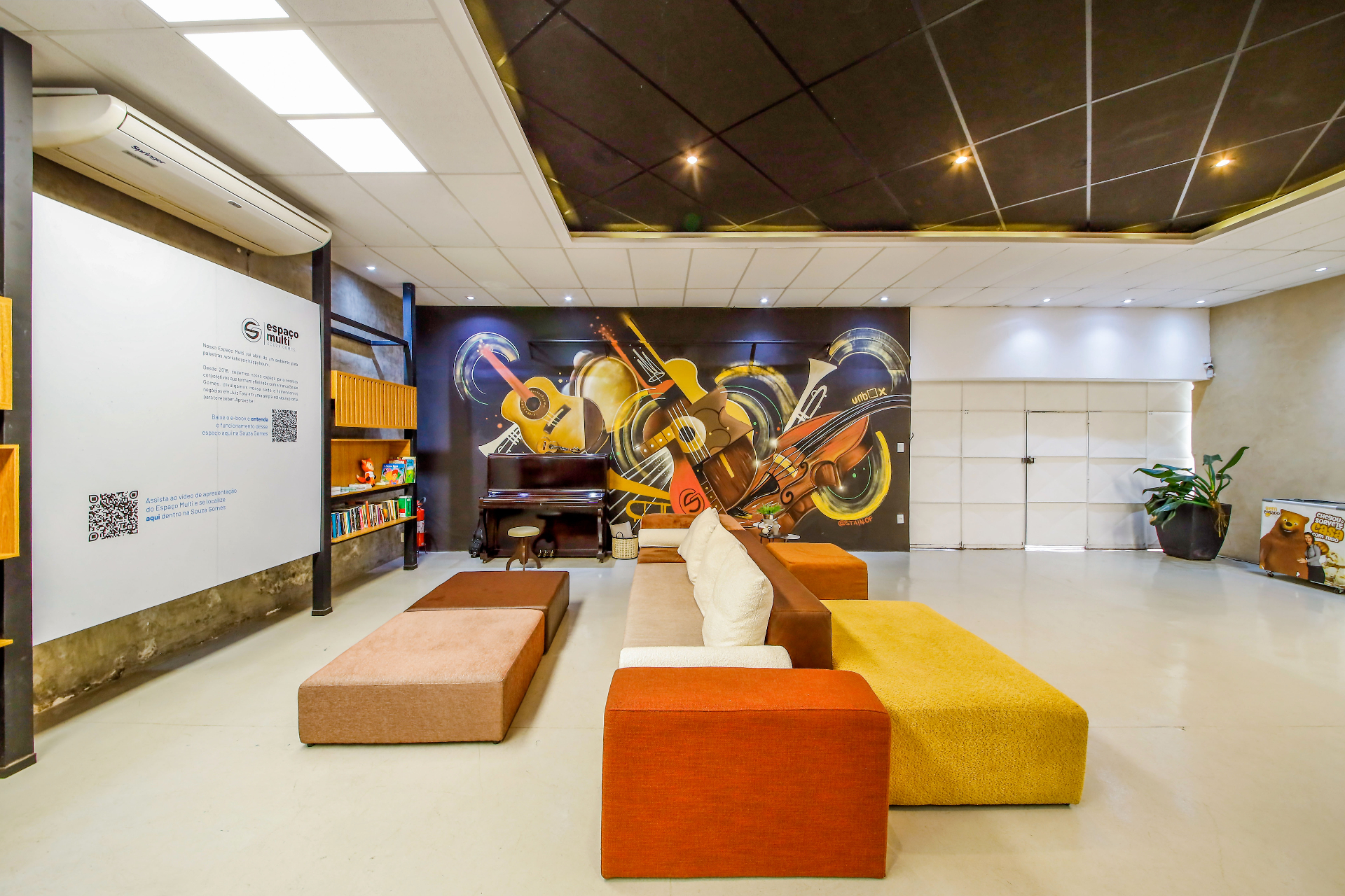 Espaço Multi: lounge com mural artístico, piano e mobiliário modular em tons quentes